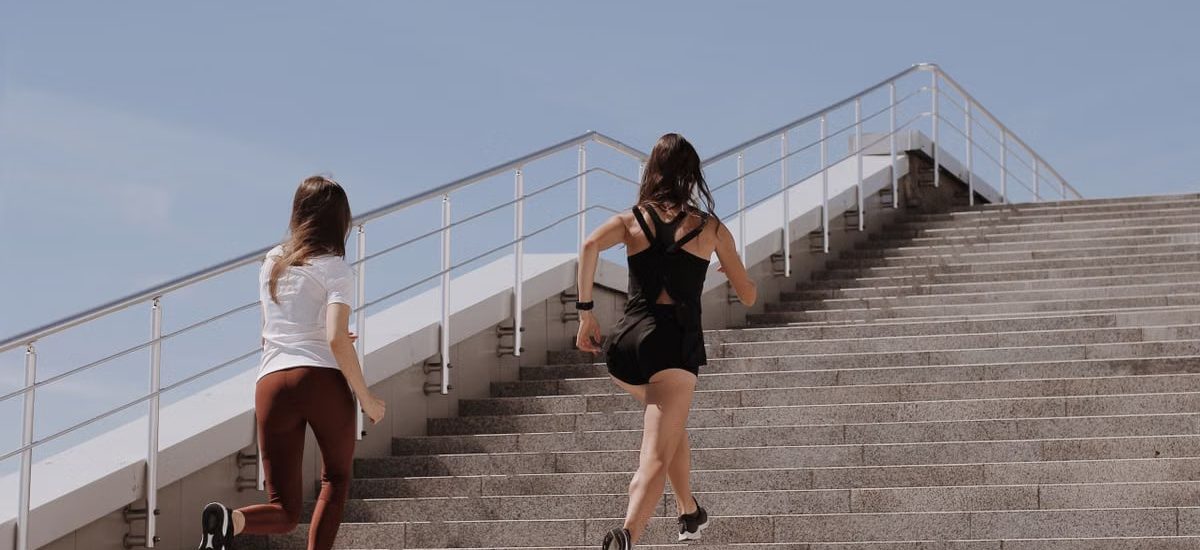 Two women running up stairs outdoors, embodying fitness and wellness.